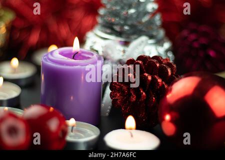 Candela a pilastri viola o lilla illuminata con ornamenti natalizi come i Baubles Pine Cone Cherries e la pelliccia rossa sullo sfondo. Tema per Merry Foto Stock