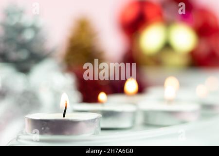 Candele TeaLight bianche illuminate in fila con colorate decorazioni Blur Bokeh su sfondo rosa chiaro. Tema per buon Natale e Felice anno nuovo Foto Stock