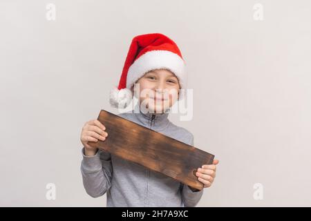 Ragazzo sorridente nel cappello di babbo natale, con un segno orizzontale vuoto di legno e spazio copia Foto Stock