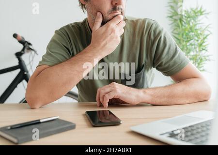 Telelavoro seduto alla scrivania di casa e pensare con mano sul mento per attività di lavoro remoto, fuoco selettivo Foto Stock