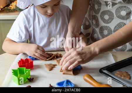 Felice madre e figlia che tagliano varie forme di biscotti in cucina. Mamma e figlia fanno biscotti di pan di zenzero a casa e Buon divertimento. Casa Foto Stock