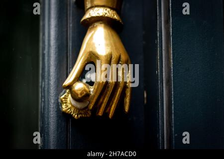 Mano d'oro che tiene una porta manopola a una porta bussare a Londra Foto Stock