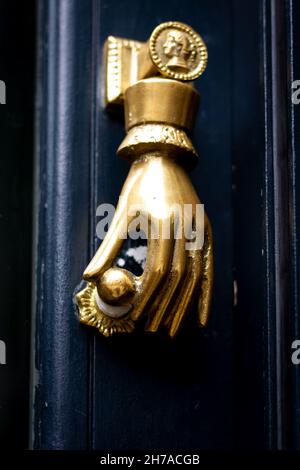 Mano d'oro che tiene una porta manopola a una porta bussare a Londra Foto Stock