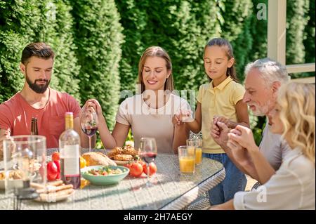 Una famiglia che tiene le mani e prega prima di cena Foto Stock