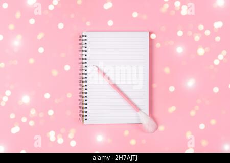 Blocco note e penna rosa decorata con piuma su sfondo rosa. Concetto di lista dei desideri di vacanza Foto Stock