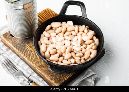 Set di fagioli bianchi in scatola, con lattina metallica, in padella di ghisa, su superficie di pietra bianca Foto Stock