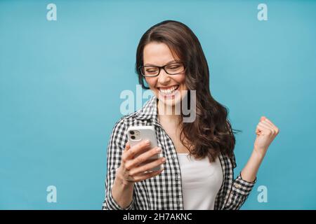 Bruna felice eccitato guardando lo schermo del telefono, celebrando la vittoria in linea, ragazza allegra urlando di gioia, tenendo smartphone, leggendo bene Foto Stock
