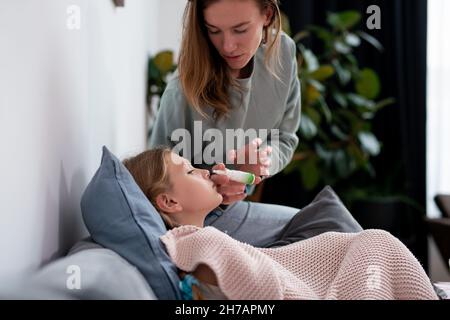 Madre spray nasale farmaci per la figlia malata. Foto Stock