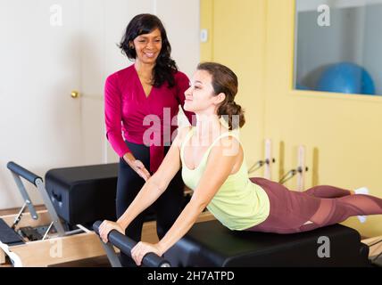 Ispanica femmina pilates istruttore aiutare la donna che si esercita sul reformer Foto Stock