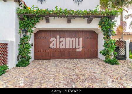 Porte da garage doppie in legno scuro con cerniera laterale a la Jolla, California. Esterno di un garage con piante striscianti sul pergolato annesso e un vialetto wi Foto Stock