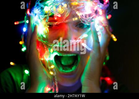 La donna si aggrappa alla testa in un panico. Ragazza di Natale stressata Screaming. Giovane che si diverte durante le vacanze invernali con luci colorate. Donna Foto Stock