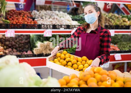 Giovane donna venditore in maschera di trasporto scatola con prugne Foto Stock