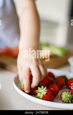 Mano di primo piano carino bambino prendendo fresco fragola rossa dal piatto di raccolta stagionale Foto Stock