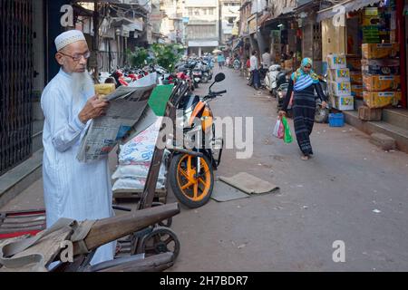Un anziano musulmano Bohra nella zona di Dongri, dominata dai musulmani, Mumbai, India, in piedi per strada leggendo un giornale Foto Stock