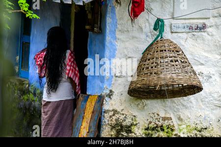 Vecchia signora del villaggio, stile di vita del villaggio tribale indiano, una gabbia di bambù fatta a mano per i polli appesi nel muro. Foto Stock