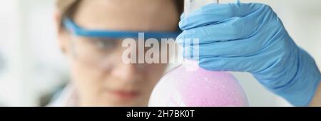 Donna scienziata che tiene in laboratorio il pallone con liquido viola con schiuma Foto Stock