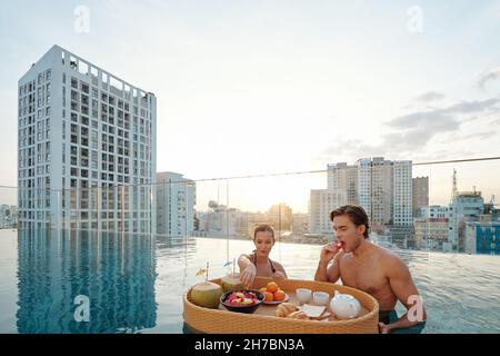 Bella giovane uomo e donna che mangiano deliziosa colazione nella piscina sul tetto Foto Stock
