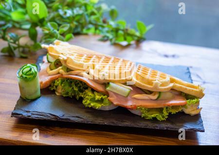 Waffle belgi con pesce e avocado sul piatto nero Foto Stock