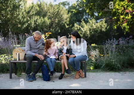 Coppia anziana con nipoti seduti su panca e facendo homewrok all'aperto nel parco. Foto Stock
