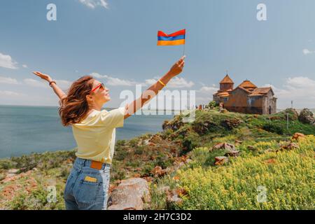Felice turista con bandiera armena che posa al Monastero di Hayravank sulla riva del Lago Sevan. Foto Stock