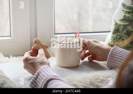Donna che beve caffè con marshmallow e biscotti pan di zenzero pupazzo di neve. Accogliente vacanza invernale. Foto Stock