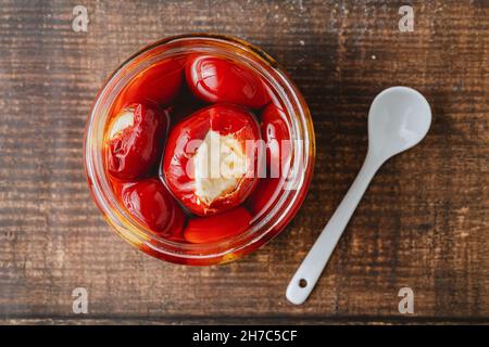 Peperoncini ripieni di ricotta ripieni in vasetto di vetro su sfondo legno Foto Stock