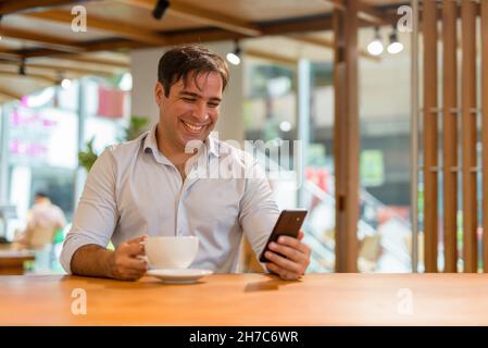Ritratto di un bel uomo persiano seduto al bar mentre si usa il telefono cellulare Foto Stock