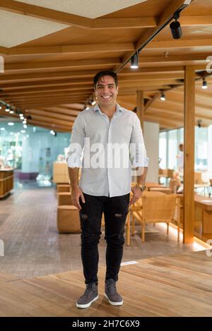 Ritratto a tutta lunghezza di un bel uomo persiano sorridente e in piedi in caffetteria Foto Stock