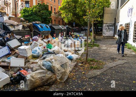 Roma, Italia. 22 novembre 2021. Un pedone passa davanti a grandi mucchi di sacchi di rifiuti in un punto di raccolta rifiuti e riciclaggio che rimane non raccolto per giorni in un sobborgo a nord di Roma . Roma è stata afflitta da una crisi di spazzatura che è durata per mesi a causa di uno sciopero da parte dei binmen e la chiusura di un grande sito di discariche che ha causato rabbia e sollevato preoccupazioni per la salute tra i residenti. Credit: amer Ghazzal/Alamy Live News Foto Stock