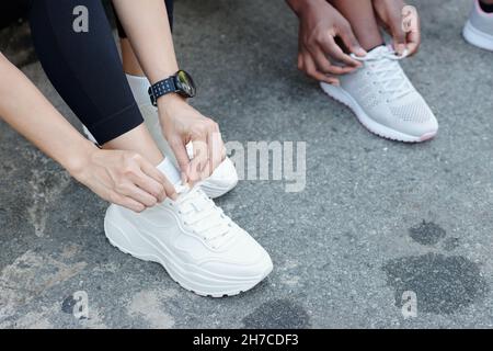 Immagine ritagliata delle giovani donne che legano le scarpe quando si preparano per la corsa mattutina all'aperto Foto Stock