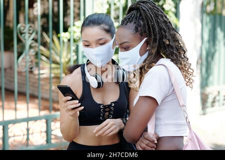 Giovani sportivi in maschere mediche utilizzando l'applicazione su smartphone per ordinare taxi auto Foto Stock