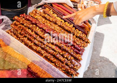 La donna sceglie una churchkhela in un mercato locale georgiano o armeno. Questo è un dessert tradizionale fatto di succo d'uva e noci su una corda Foto Stock