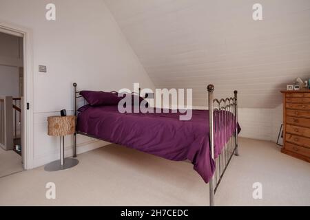 Stradeshall, Suffolk, Inghilterra - 16 giugno 2020: Camera da letto mansardata in stile loft con pareti dipinte di bianco, struttura in metallo e biancheria da letto viola Foto Stock