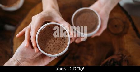 Cacao cerimoniale caldo fatto a mano in tazze bianche. Donna mani che danno cacao artigianale, vista dall'alto su tavola di legno. Bevanda biologica sana al cioccolato preparata da Foto Stock