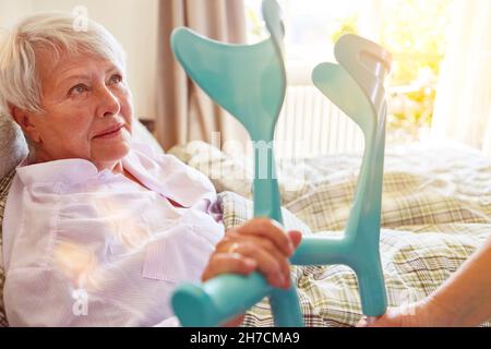 Donna anziana con stampelle come aiuto per camminare si trova a letto nella casa di cura Foto Stock