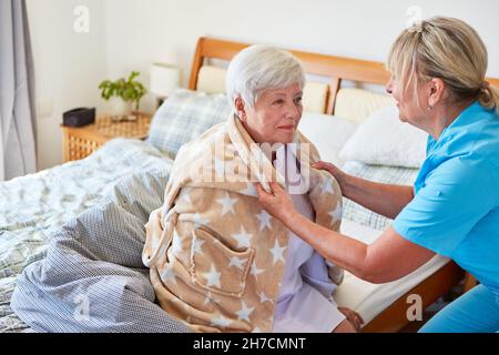 L'anziano operatore aiuta la donna anziana malata a indossare un accappatoio nella casa di riposo o a casa Foto Stock