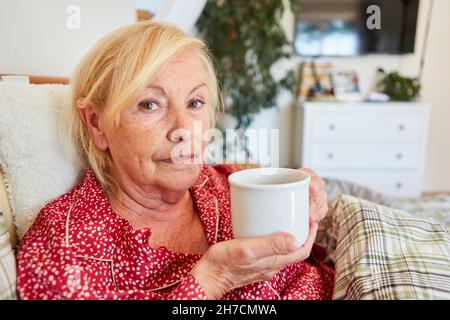 Anziano donna triste bere caffè a letto a casa o casa di riposo Foto Stock