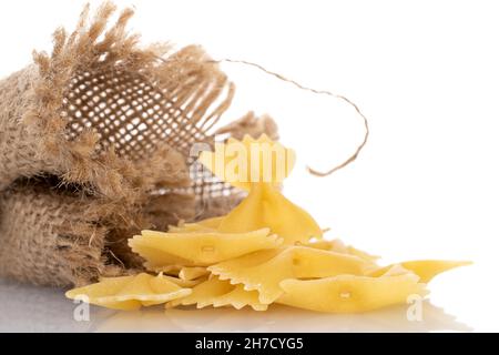 Pasta cruda di colore giallo chiaro, a forma di farfalla, con sacchetto di iuta, primo piano, isolato su bianco. Foto Stock