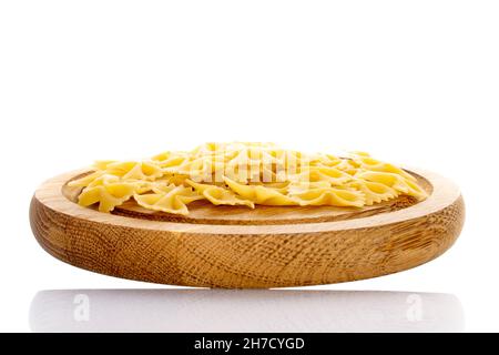 Pasta cruda giallo chiaro, a forma di farfalla, su vassoio di legno, primo piano, isolata su bianco. Foto Stock