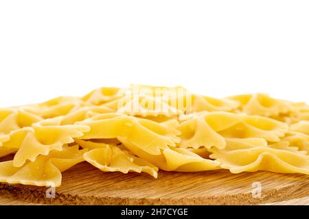 Pasta cruda giallo chiaro, a forma di farfalla, su vassoio di legno, primo piano, isolata su bianco. Foto Stock