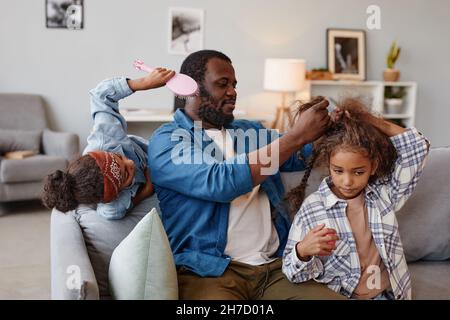 Ritratto di singolo padre afro-americano spazzolando i capelli di due ragazze carine a casa, spazio copia Foto Stock
