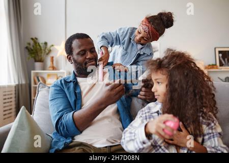 Ritratto di singolo padre afroamericano spazzolando i capelli di due figlie a casa, spazio copia Foto Stock