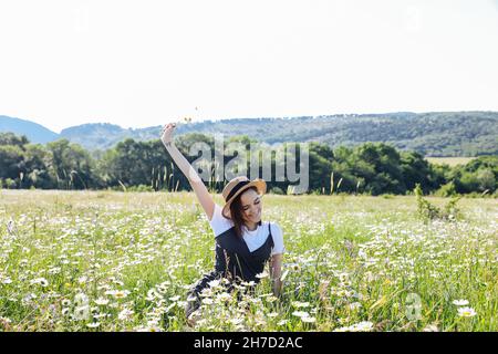 donna in un abito che cammina attraverso il campo con margherite Foto Stock