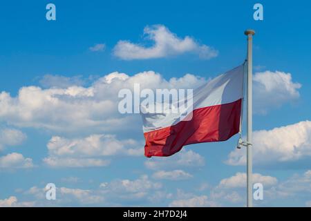 La bandiera nazionale della Polonia vola contro un cielo blu e alcune nuvole bianche. Foto Stock