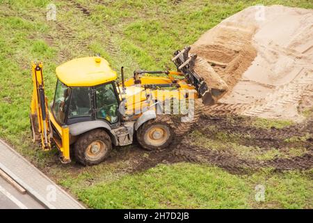 Il trattore con benna per sabbia livella la superficie accanto all'erba Foto Stock