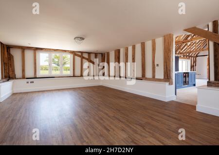 Great Sampford, Essex - Aprile 16 2020: Soggiorno vuoto all'interno di un grande fienile recentemente convertito con legno a vista e pavimento in legno con vista sulla cucina Foto Stock