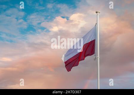 La bandiera nazionale della Polonia vola su uno sfondo di cielo blu e nuvole color pesca. Foto Stock