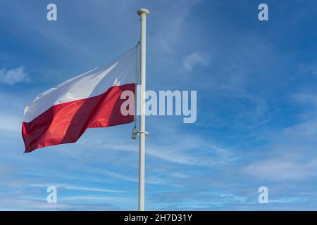 La bandiera nazionale della Polonia vola contro un cielo blu e alcune nuvole bianche. Foto Stock