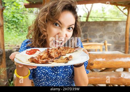 Una donna con un appetito brutale mangia e morde una deliziosa bistecca di manzo. Il concetto di carnivoro e fame Foto Stock