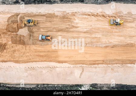 il bulldozer giallo e i rulli stradali lavorano in cantiere, livellando il terreno per la strada futura. vista dall'alto aerea. Foto Stock